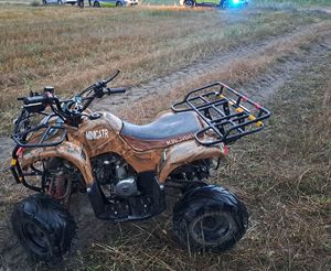 Pojazd quad stojący na polu koloru żółtego w tle radiowozy policji.