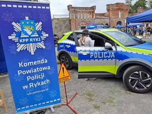 Baner Komendy Powiatowej Policji w Rykach i oznakowany radiowóz policyjny