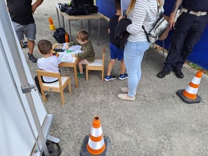 Dzieci siedzące przy stoliku rysują. obok stoi kobieta.