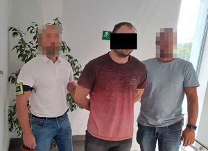 Policjanci prowadzą zatrzymanego poszukiwanego mężczyznę  z założonymi kajdankami