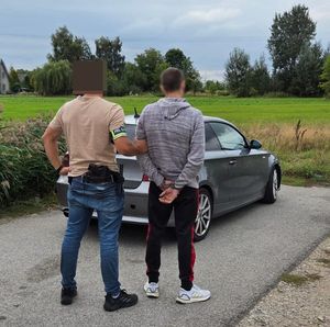 Policjanci prowadzą zatrzymanego poszukiwanego mężczyznę  z założonymi kajdankami