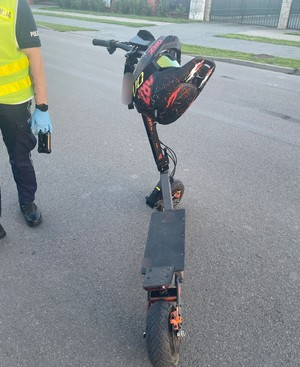 hulajnoga elektryczna stojąca na jedni obok sylwetka policjanta umundurowanego w kamizelce odblaskowej