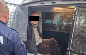 Osoba zatrzymana siedząca w radiowozie typu bus obok stoi policjant umundurowany