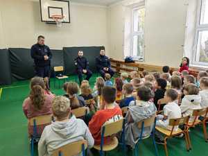 Policjanci prowadzą prelekcje dla grupy dzieci siedzących na sali gimnastycznej