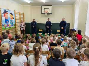 Policjanci prowadzą prelekcje dla grupy dzieci siedzących na sali gimnastycznej