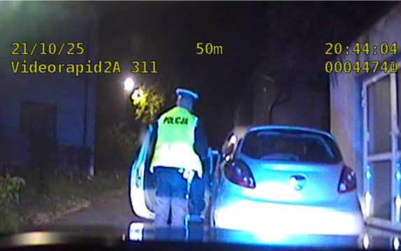 Na zdjęciu policjanci na ulicy w porze nocnej  dokonują kontroli trzeźwości kierującego siedzącego w pojeździe osobowym koloru szarego.