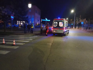 Miejsce zdarzenia drogowego w tle kareta pogotowia obok niej ratownik i kobieta, na zdjęcie jest umundurowany policjant który rozmawia dwoma mężczyznami w tle budynki i przejście dla pieszych