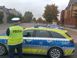 Policjant stoi obok radiowozu i nadzoruje ruch.