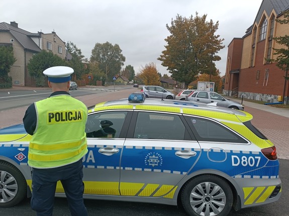Policjant stoi obok radiowozu i nadzoruje ruch.