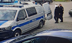 Policjant prowadzi zatrzymanego do radiowozu policji