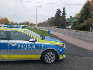Radiowóz oznakowany i policjant stoi przy drodze i nadzoruje ruch
