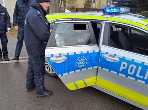 policjanci wykonują czynności  za trzymanym mężczyzna siedzącym w radiowozie policjanci stoją obok otwartych drzwi radiowozu