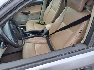 wnętrze samochodu osobowego z jasna tapicerka. Na fotelu kierowcy zapięte pasy na fotelu pasażera leży butelka z piwem koloru zielonego