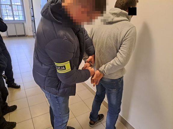 Policjant nieumundurowany z opaską z napisem policja zakłada kajdanki zatrzymanemu mężczyźnie