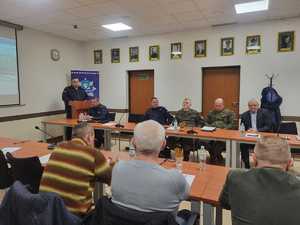 Uczestnicy debaty siedzący na krzesłach w sali konferencyjnej przemiaiwa nadkomisarz Łukasz Walo