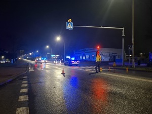Zdjęcia z miejsca wypadku drogowego., Widoczna jest droga na której ustawione są znaki zabezpieczające oraz pojazdy w tym służb ratunkowych. Zdjęcie w porze nocnej. Ruchem kieruje żołnież żandarmerii wojskowej.
