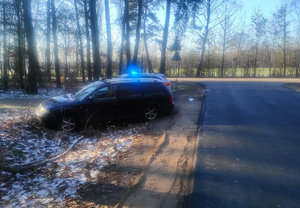 Samochód marki Volkswagen koloru granatowego stojący w rowie przydrożnym obok radiowóz policji