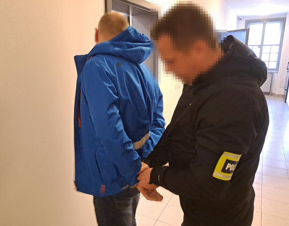 Zatrzymany mężczyzna ma zakładane kajdanki na ręce z tyłu przez policjanta