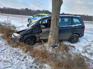 Pojazd marki Opel uszkodzony w wyniku zadurzenia z drzewem obok stoi radiowóz policji na droga jest zaśnieżona i oblodzona