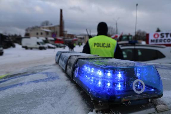 Radiowóz policji z włączonymi sygnałami w tle policjant i ciągniki rolnicze