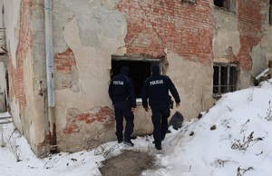 Dwóch policjantów sprawdza miejsca gdzie mogą przebywać osoby narażone na wychłodzenie w tle widoczny opuszczony budynek