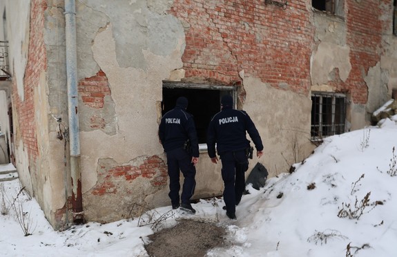 Dwóch policjantów sprawdza miejsca gdzie mogą przebywać osoby narażone na wychłodzenie w tle widoczny opuszczony budynek