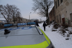 Dwóch policjantów sprawdza miejsca gdzie mogą przebywać osoby narażone na wychłodzenie w tle widoczny opuszczony budynek