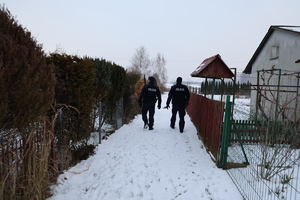 Dwóch policjantów sprawdza miejsca gdzie mogą przebywać osoby narażone na wychłodzenie w tle widoczne domki na ogródka działkowych