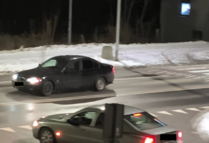 BMW koloru ciemnego stoi na ulicy z włączonym kierunkowskazem w tle zbudowania i inne pojazdy