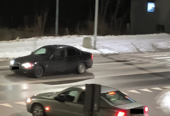 BMW koloru ciemnego stoi na ulicy z włączonym kierunkowskazem w tle zbudowania i inne pojazdy