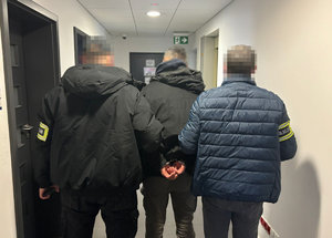 Zatrzymana osoba poszukiwana prowadzona przez dwóch  policjantów pionu kryminalnego