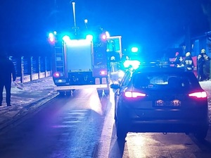 Zdjęcia z miejsca zdarzenia drogowego. widoczna jest ulica o nawierzchni asfaltowej na której stoją pojazdy policji i straży z włączonymi światłami błyskowymi w tle zabudowa miejska. Zdjęcie w porze nocnej.