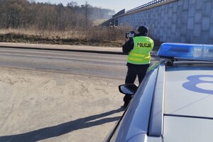 Policjant podczas pomiaru prędkości obok stoi radiowóz w tle droga