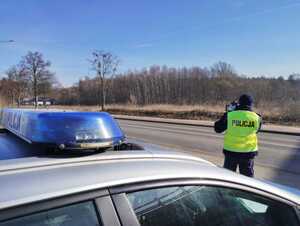 Policjant podczas pomiaru prędkości obok stoi radiowóz w tle droga