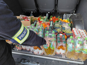 Produkty spożywcze ustawione w bagażniku buza obok widoczny jest ręka z opaską policja na ramieniu