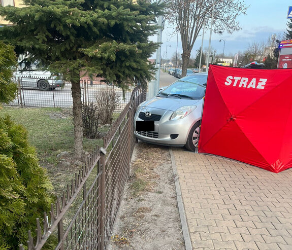samochód marki toyota stoi przy wygiętym ogrodzeniu posesji. Obok jest rozłożony parawan z napisem straż.
