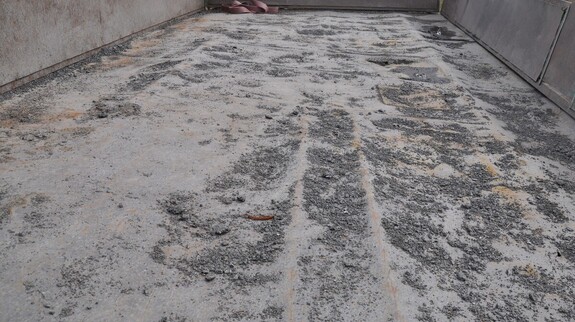 Skrzynia ładunkowa przyczepy z rozsypanymi drobinami destruktu asfaltowego na podłodze