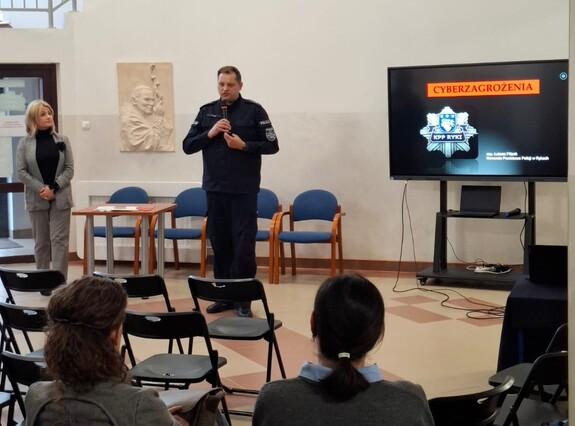 Policjant podczas prelekcji w szkole trzyma w ręku mikrofon.