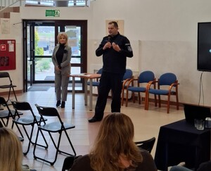 Policjant podczas prelekcji w szkole trzyma w ręku mikrofon.