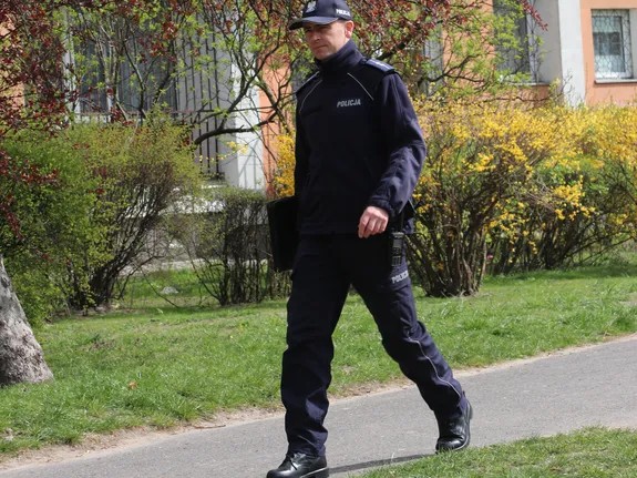 Umundurowany policjant idzie chodnikiem w tle zabudowa miejska