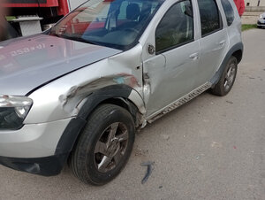 Uszkodzony samochód osobowy marki dacia stojący na drodze. Pojazd ma uszkodzony lewy  bok w przedniej części.