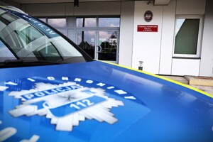 Radiowóz policyjny jego przód z odznaką policyjną na pokrywie silnika w tle budynek Komendy Powiatowej Policji w Rykach