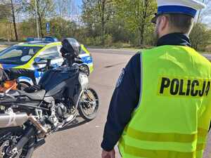 Policjant podczas kontroli drogowej obok stoi motocykl a za nim radiowóz
