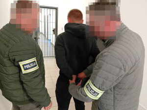 Policjant zakłada kajdanki na ręce trzymane z tyłu zatrzymanemu mężczyźnie drugi policjant stoi obok.