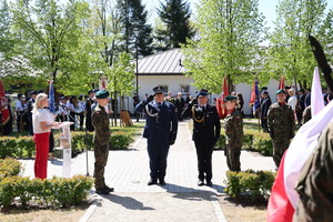 nadkomisarz Łukasz Walo Komendant  Powiatowy Policji w Rykach oddaje hołd salutując wraz w brygadierem Krzysztofem Ambrożkiem przez pomnikiem w tle uczestnicy uroczystości