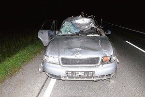 Samochód osobowy marki Audi z uszkodzonym przodem i dachem i szybą czołową stoi n drodze w tle funkcjonariusz policji