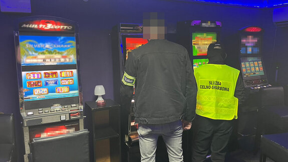 Policjant i funkcjonariusz służby celno-skarbowej stoją przy automatach do gier