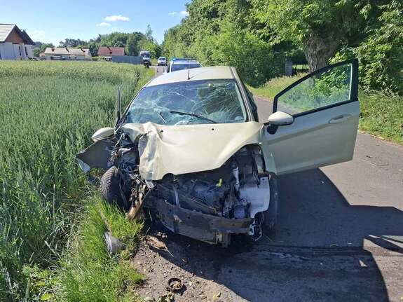 Samochód osobowy marki Ford z uszkodzonym przodem stoi na jezdni asfaltowej w tle widać zabudowania i pola uprawne