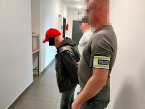 Dwóch policjantów prowadzi  korytarzem zatrzymanego mężczyznę