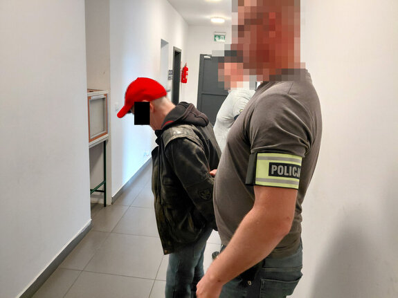 Dwóch policjantów prowadzi  korytarzem zatrzymanego mężczyznę